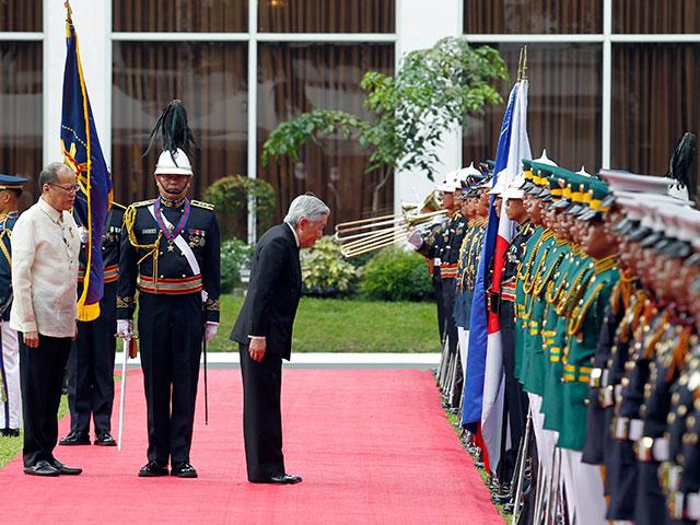 Emperor Akihito bows to the Philippine and Japanese flags during arrival honors accorded him as a state visitor in Malacanang. MALACANANG PHOTO BUREAU