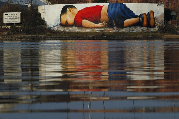 A huge graffiti artwork of toddler Aylan Kurdi, by Frankfurt artists Justus Becker and Oguz Sen is seen on a wall on the banks of river Main near the headquarters of the European Central Bank in Frankfurt, Germany, March 10, 2016. The huge graffiti image of toddler Aylan Kurdi, pictures of whose dead body stirred global sympathy for migrants fleeing war and poverty, confronts motorists, pedestrians and river travellers in Frankfurt. The artwork of the three-year-old Syrian boy, who drowned in September along with his mother and brother as they tried to reach Europe, will stay on the peninsula, about a 15-minute walk from the city centre, until autumn. The graffiti's creators are two artists who also go by the names of COR and Bobby Borderline. Photo: REUTERS/Kai Pfaffenbach
