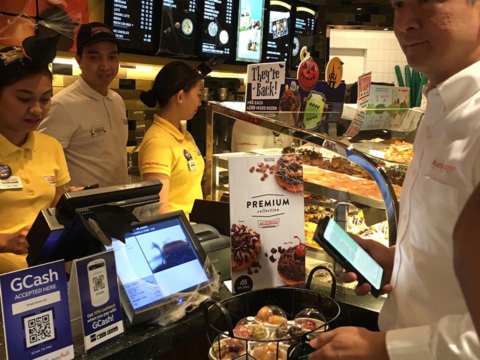 Caption: MGI chief financial officer Dave Fuentebella tries GCash's scan-to-pay feature at Krispy Kreme
