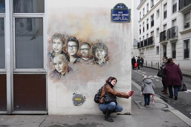 A woman takes a selfie with portraits (L to R) of late French satirical weekly Charlie Hebdo's deputy chief editor Bernard Maris, French cartoonists Georges Wolinski, Bernard Verlhac (aka Tignous), Charlie Hebdo editor Stephane Charbonnier (aka Charb) and Jean Cabut (aka Cabu) painted on a facade near the magazine's offices at Rue Nicolas Appert, in Paris on January 7, 2018, on the third anniversary of the jihadist attack on French satirical magazine Charlie Hebdo. Christophe Archimbault/AFP