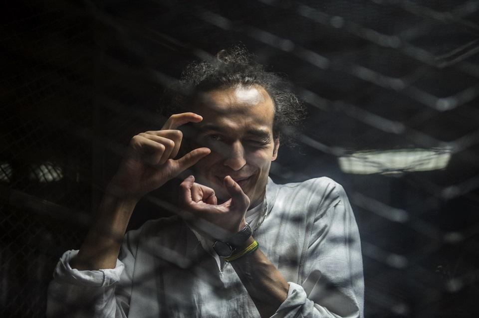 Egyptian photographer Mahmoud Abdel Shakour, known as Shawkan, gestures from inside a soundproof glass dock, during his trial in the capital Cairo on August 9, 2016, Shawkan had been covering the police dispersal of an Islamist protest camp in Cairo when he was arrested and has been in prison ever since. Thousands of Islamists remain in prison in a wideranging crackdown that has extended to leftists and even journalists like Shawkan. Khaled Desouki/AFP