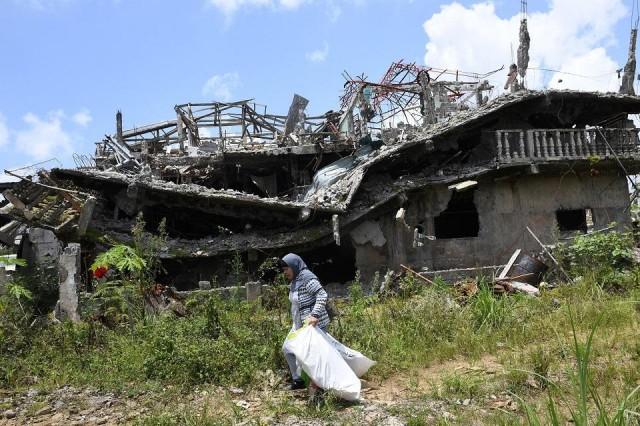 A resident carrying salvaged belongings walks past destroyed buildings during a visit to the main battle area in Marawi City on April 1, 2018. Ted Aljibe/AFP