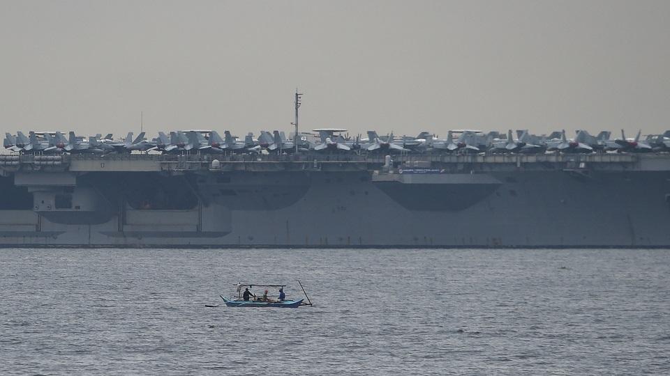 Fishermen aboard their wooden boat sail past the nuclear-powered aircraft carrier USS Ronald Reagan (CVN-76), anchored off Manila Bay on June 26, 2018, the third such call by a US carrier in four months, as its admiral hailed America's "enduring presence" in a region where China's military build-up had raised tensions. Ted Aljibe/ AFP