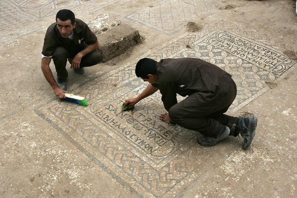 Israeli prisoners clean an early Christian mosaic in the ruins of a recently excavated rare church from the 3rd-4th centuries AD in the grounds of Megiddo Prison in northern Israel on November 6, 2005. A mosaic inscription on the floor declared that the structure had been dedicated to the God Jesus Christ as a memorial. Menahem Kahana/AFP