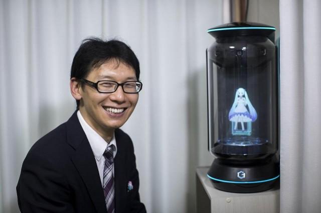 In this photograph taken on November 10, 2018 Japanese Akihiko Kondo poses next to a hologram of Hatsune Miku at his apartment in Tokyo, a week after 'marrying' her. Kondo, a school administrator 'married' the computer animation with saucer eyes and lengthy aquamarine pigtails that performs to adoring fans as virtual reality character. Behrouz Mehri/AFP