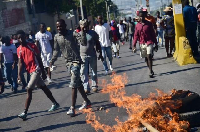 Demonstrators carry rocks as they march past burning tires on the fifth day of protests in Port-au-Prince, February 11, 2019, against Haitian President Jovenel Moise and the misuse of Petrocaribe funds. HECTOR RETAMAL / AFP