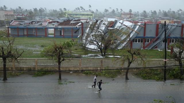 People walk down a flooded road next to buildings damaged by Cyclone Idai in Beira, Mozambique, March 17, 2019 in this still image taken from a social media video on March 18, 2019. International Federation Of Red Cross And Red Crescent Societies via REUTERS