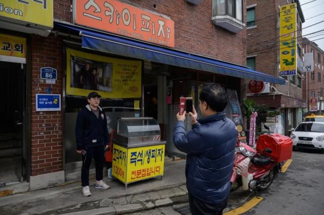 A customer poses before a photo of film director Bong Joon-ho at the 'Sky Pizza' restaurant in Seoul on February 13, 2020. ED JONES / AFP