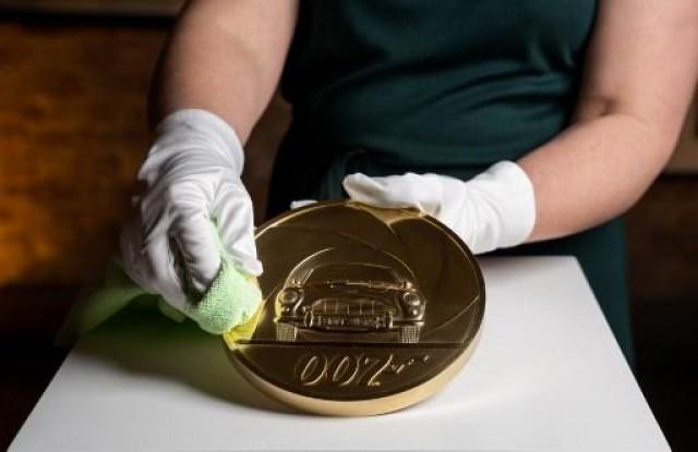 A handout picture released by the Royal Mint in London on March 2, 2020, shows Royal Mint designer Laura Clancy posing with a special edition James Bond themed seven kilogram Gold Proof coin, to celebrate the upcoming release of the 25th James Bond film. Royal Mint / AFP