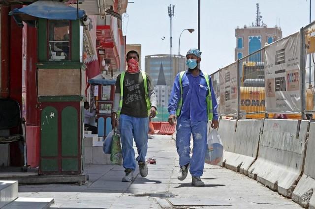 Workers wearing protective masks walk by on a street in Qatar's capital Doha, on May 17, 2020, as the country begins enforcing the world's toughest penalties for failing to wear masks in public, as it battles one of the world's highest coronavirus infection rates. Violators of the new rules will face up to three years in jail and fines of as much as $55,000. Karim Jaafar/AFP