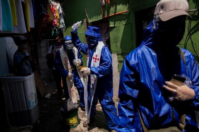 Fr. Eduardo "Ponpon" Vasquez Jr, 47, wears personal protective equipment as he sprinkles holy water on the narrow streets of a slum area, during the government-imposed lockdown to contain the coronavirus disease (COVID-19) outbreak, in Caloocan, Metro Manila, Philippines, April 22, 2020. REUTERS/Eloisa Lopez