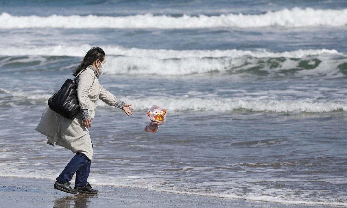 A woman throws flowers into the sea to mourn victims of March 11, 2011 earthquake and tsunami in Minamisoma, Fukushima prefecture, Japan, March 11 2021, to mark the 10-year anniversary of the disaster that killed thousands and set off a nuclear crisis. Mandatory credit Kyodo/via REUTERS