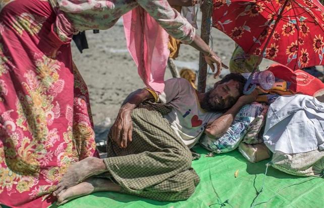 A very sick man is shielded from the sun by his wife at a border crossing in Bangladesh. Refugees have to wait a few days, usually exposed to the elements, before they are allowed to go to the transit centres and refugee camps. Atom Araullo