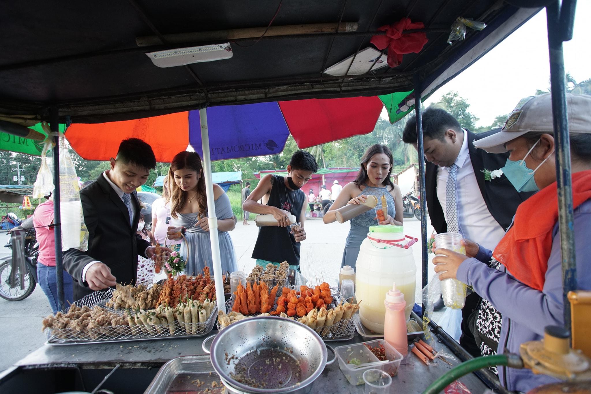 Pasangan pengantin baru melakukan pemotretan pasca-pernikahan di kios makanan jalanan Pinoy dengan rombongan