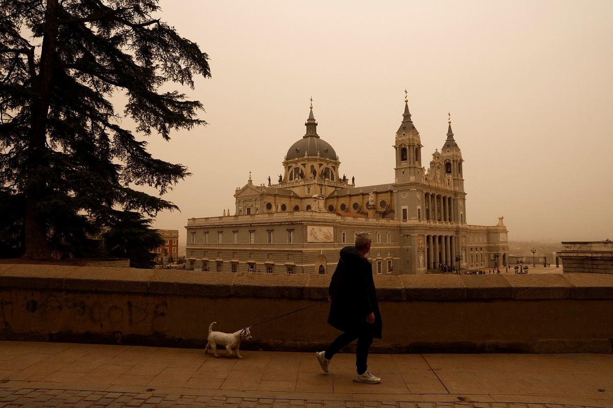 Un hombre pasea a su perro cerca de la Catedral de la Almudena, mientras la tormenta Celia soplaba arena del desierto del Sahara sobre Madrid, España, el 15 de marzo de 2022. REUTERS/Susana Vera