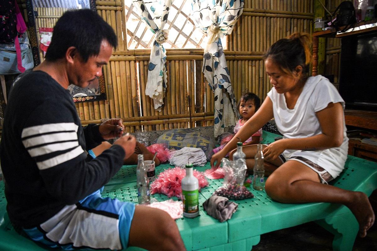 Sur cette photo prise le 9 août 2022, le pêcheur Mariel Villamonte et sa femme Shiene fabriquent des appâts dans leur maison de Barangay Cato, ville d'Infante, province de Pangasinan.  Ted Aljibe / AFP