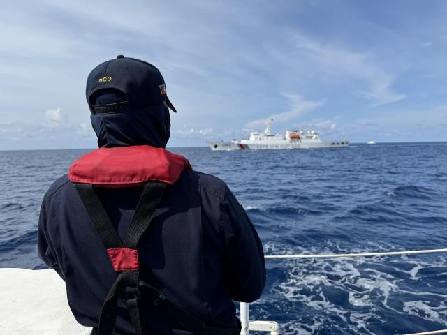 A member of the Philippine Coast Guard looks on as a Chinese ship patrols the waters off Escoda Shoal.
