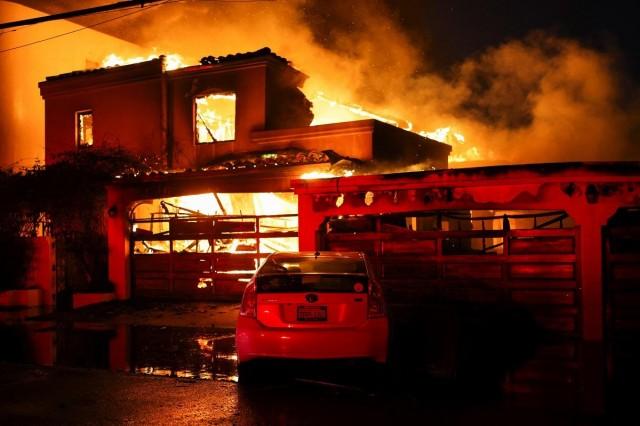 Smoke and flames rise from a burning home, as powerful winds fueling devastating wildfires in the Los Angeles area force people to evacuate, in Malibu, California, January 8, 2025. REUTERS/ Daniel Cole