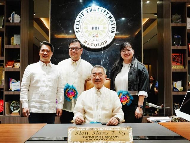 Honorary Mayor Hans Sy takes over the official city executive&acirc;s seat, with his children Harvey and Hanna Carinna (2nd and 3rd from left) standing alongside Bacolod Mayor Albee Benitez.