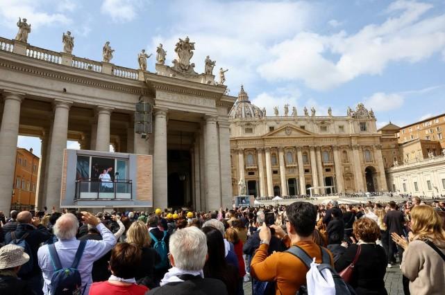 People watch Pope Francis appear from a window of Gemelli Hospital during his first public appearance in five weeks, on a big screen in St. Peter's Square, at the Vatican, March 23, 2025. REUTERS/ Ciro de Luca