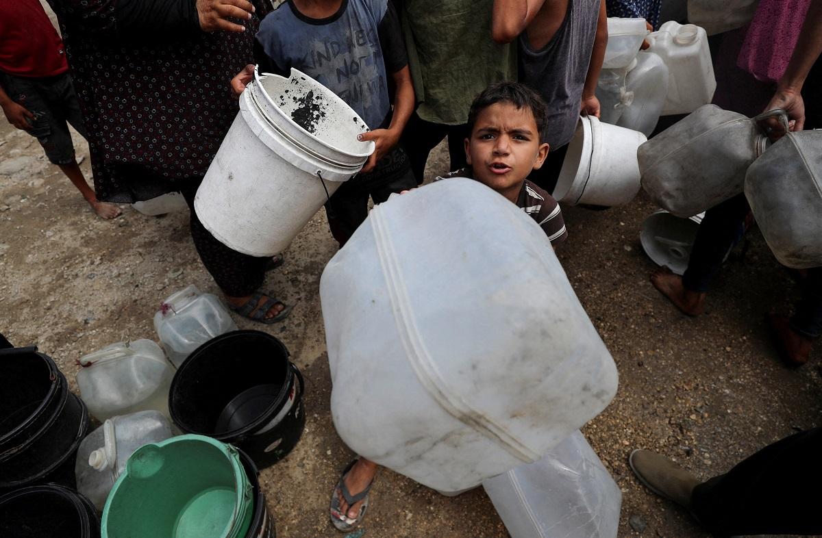 A displaced Palestinian boy waits to fill water containers at a tent camp in Gaza City