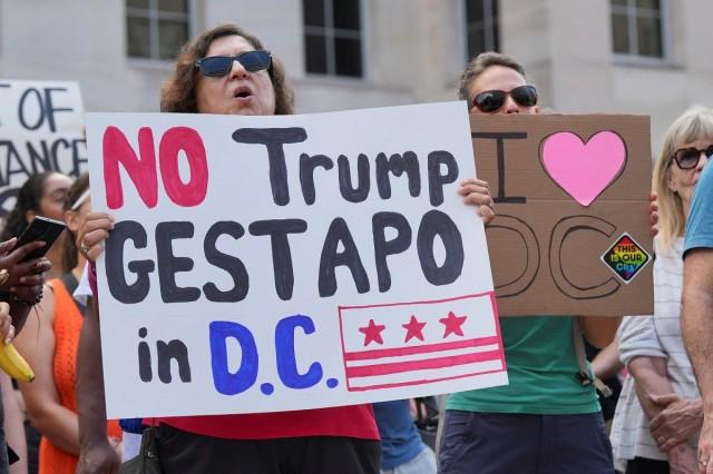 A demonstrator holds a sign during a protest near the White House, as US President Donald Trump announced he is placing the D.C. Metropolitan Police Department under direct federal control and deploying National Guard troops to the US capital, in Washington D.C., August 11, 2025. REUTERS/ Ken Cedeno
