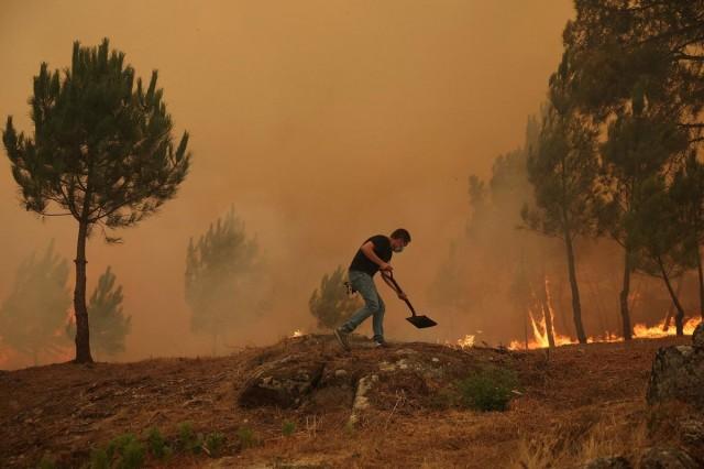A man holds a shovel as a wildfire approaches Trancoso, Portugal, August 12, 2025. REUTERS/ Pedro Nunes