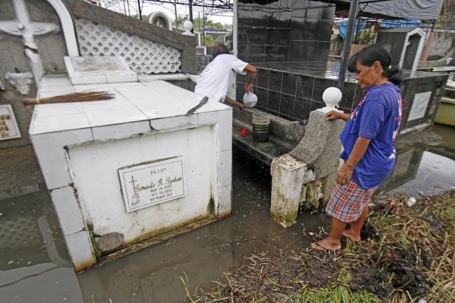 A couple cleans a loved one's tomb in a flooded part of Wakas Memorial Cemetery in Kawit, Cavite, on Thursday, October 30, 2025. Many Filipinos going to cemeteries for Undas will have to deal with stagnant floodwaters, a longtime problem across the country. DANNY PATA