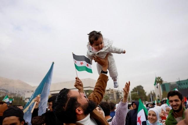 A man holds up a baby as people gather to celebrate the first anniversary of Bashar al-Assad's fall, at Ummayad Square in Damascus, Syria, December 8, 2025. REUTERS/ Yamam al Shaar