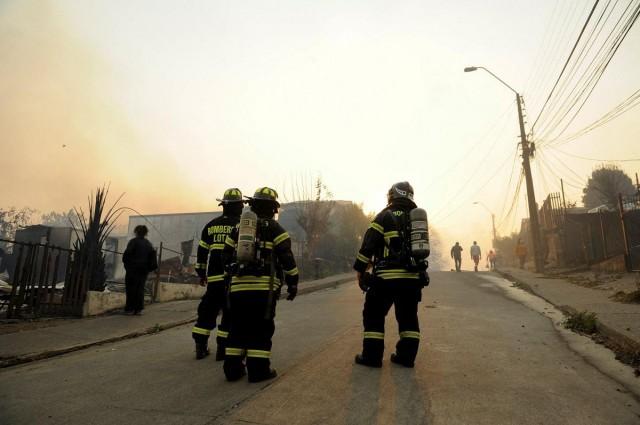 Firefighters stand on a road next to damaged buildings after a forest fire that prompted multiple emergency evacuations, in Lirquen, near Concepcion, Chile January 18, 2026. REUTERS/ Jose Luis Saavedra