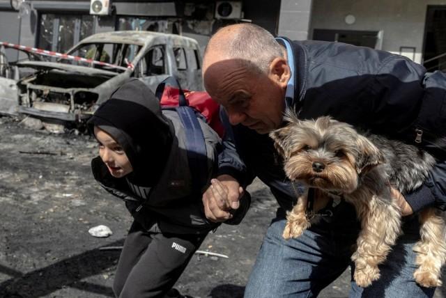 Residents carry a dog as they run from an apartment building to avoid falling glass shards after it was damaged during a night of Russian missile and drone strikes, amid Russia's attack on Ukraine, in Shchaslyve, outside Kyiv, Kyiv region, Ukraine May 14, 2026. REUTERS/ Thomas Peter
