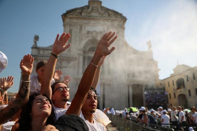 People raise their hands as they cool off in water mist outside the Basilica of Santa Maria degli Angeli while gathering for Pope Leo's visit marking the 800th anniversary of the death of St. Francis, during a heatwave in Assisi, Italy, August 6, 2026. REUTERS/ Antonio Denti