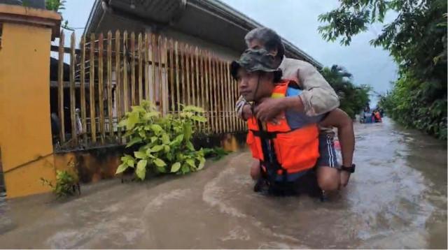 A rescuer carries a resident on his back through waist-deep floodwaters.