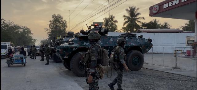 Two armored personnel carriers and Special Action Force troopers stand guard several meters from a polling center in Shariff Saydona Mustaphaa