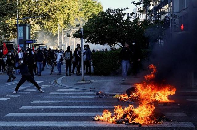 A demonstrator throws an object over burning trash containers during a demonstration by French high school and university students in Strasbourg, France, October 6, 2026. REUTERS/ Kai Pfaffenbach